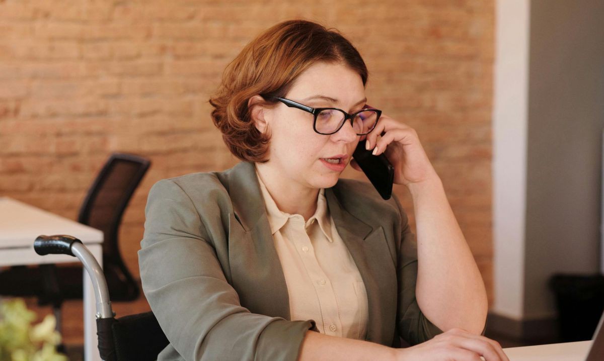 Frau im Rollstuhl sitzt am Schreibtisch und telefoniert.