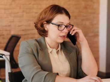 Frau im Rollstuhl sitzt am Schreibtisch und telefoniert.