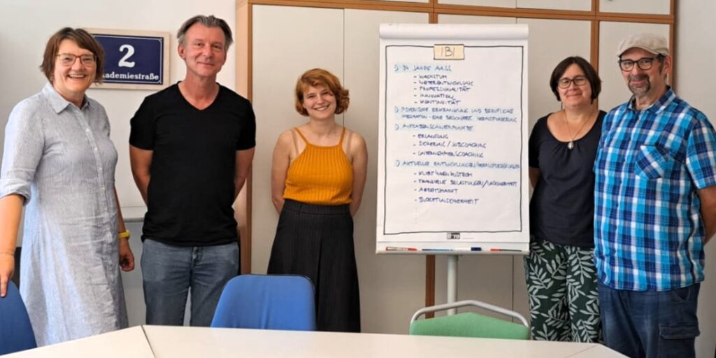 Fünf Personen stehen nebeneinander in einem Büro von IBI. Zwiscchen ihnen ist ein beschriebenes Flipchart platziert.