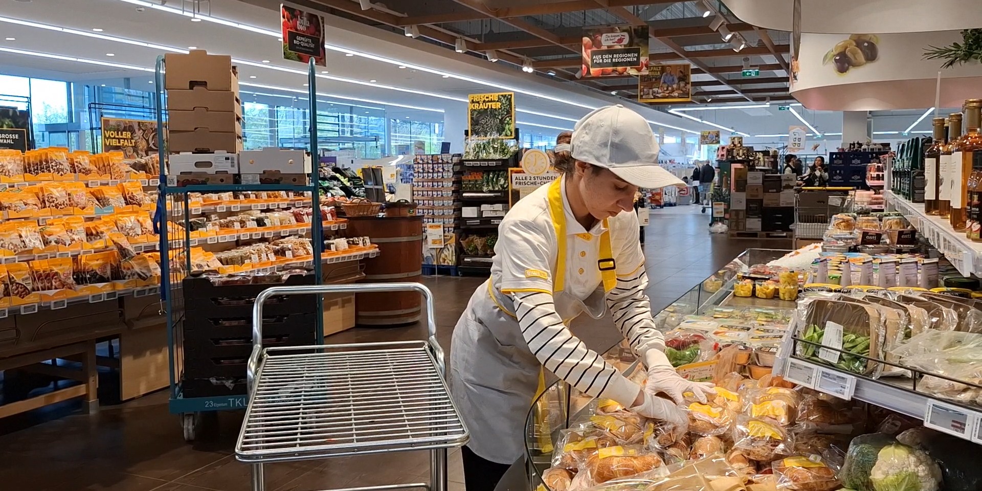 Junge Frau räumt in einem Supermarkt Snacks in ein Frischeregal.