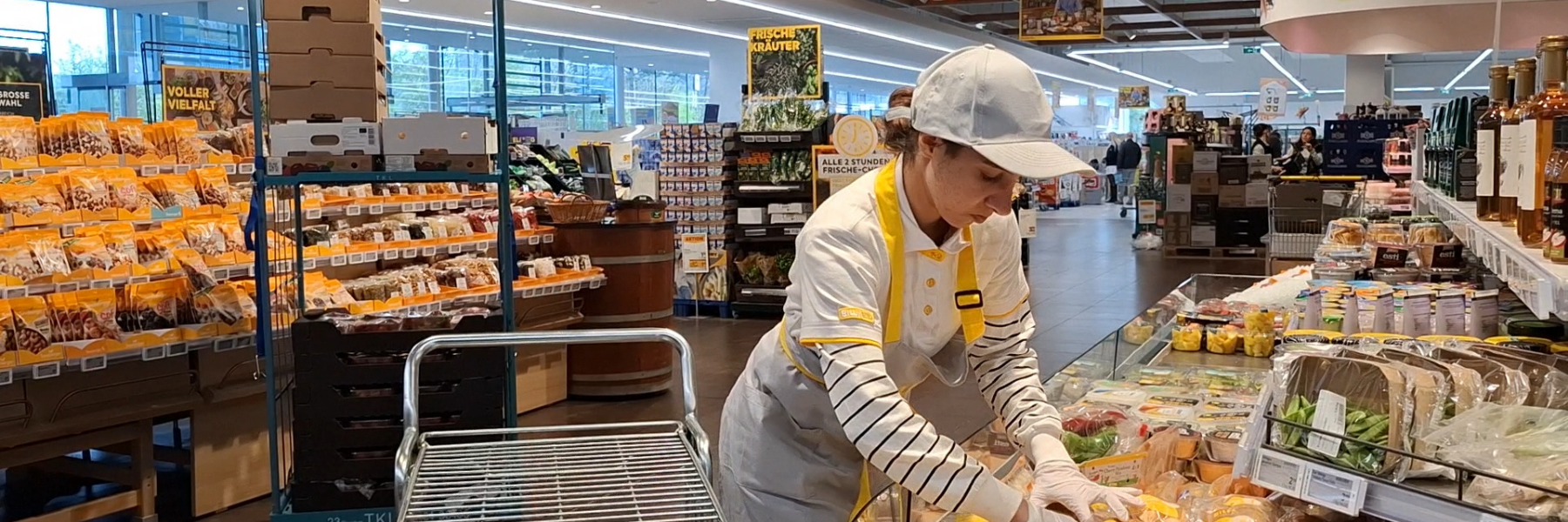Junge Frau räumt in einem Supermarkt Snacks in ein Frischeregal.