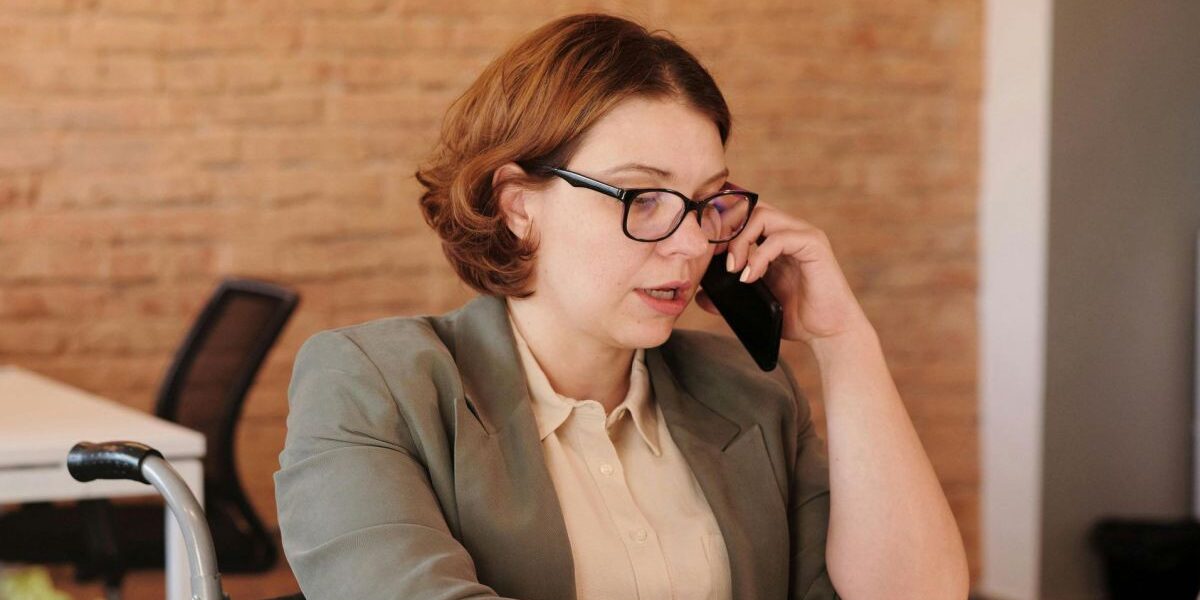 Frau im Rollstuhl an einem Büroarbeitsplatz während eines Telefonats.