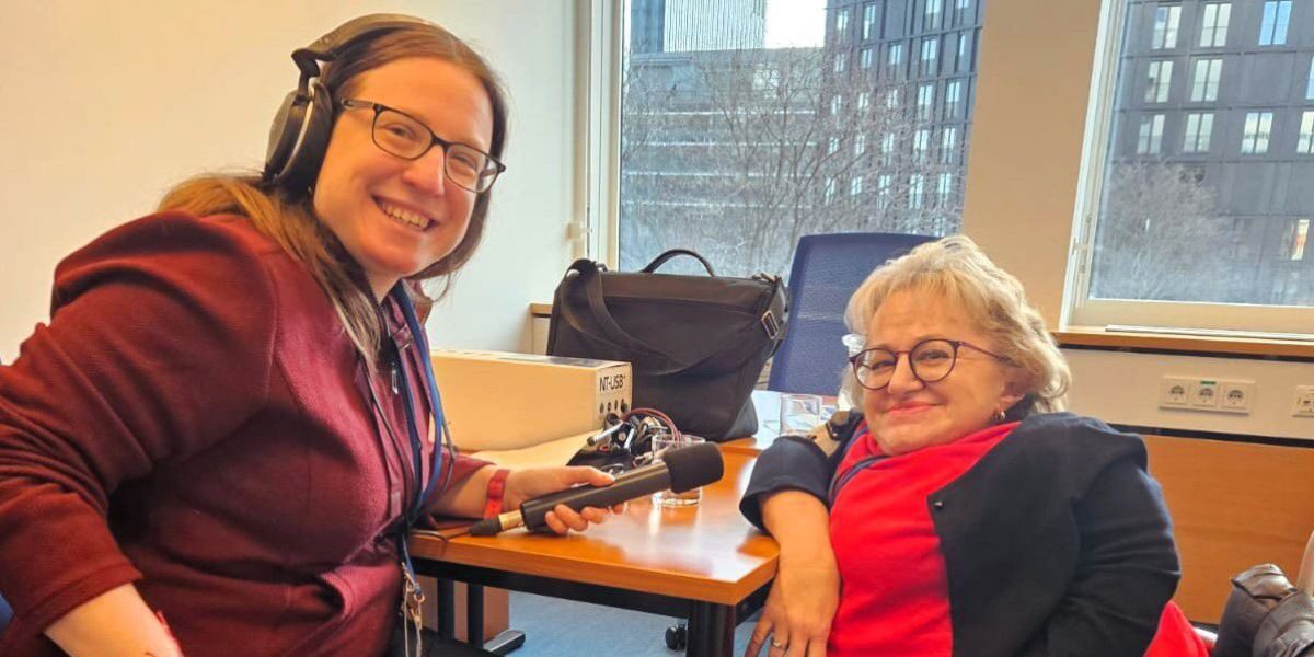 Karin Stöckler sitzt im Rollstuhl an einem Tisch beim Interview mit Podcasterin Sandra Knopp.